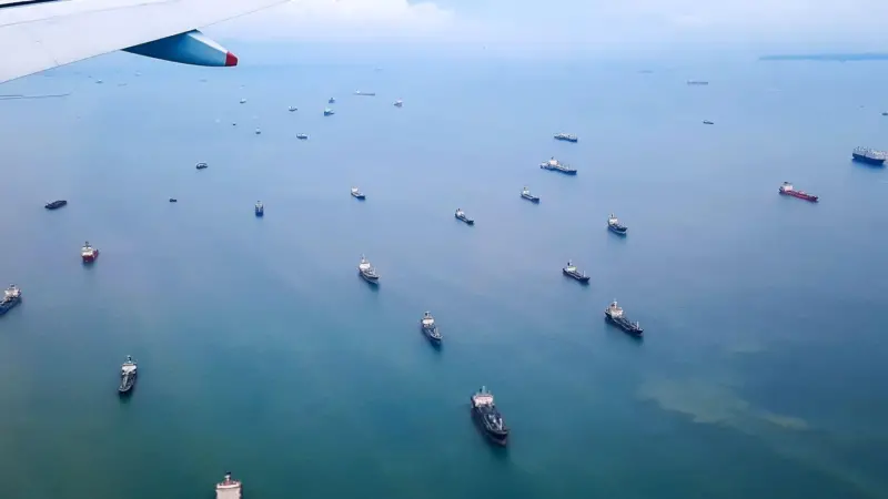 aircraft wing over ocean with a fleet of ships