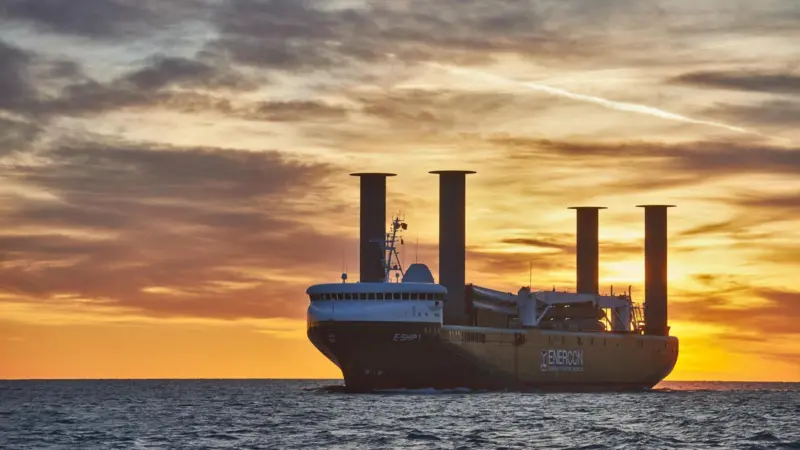 Wind-assisted cargo ship with four Flettner rotor sails at sea with a sunset behind
