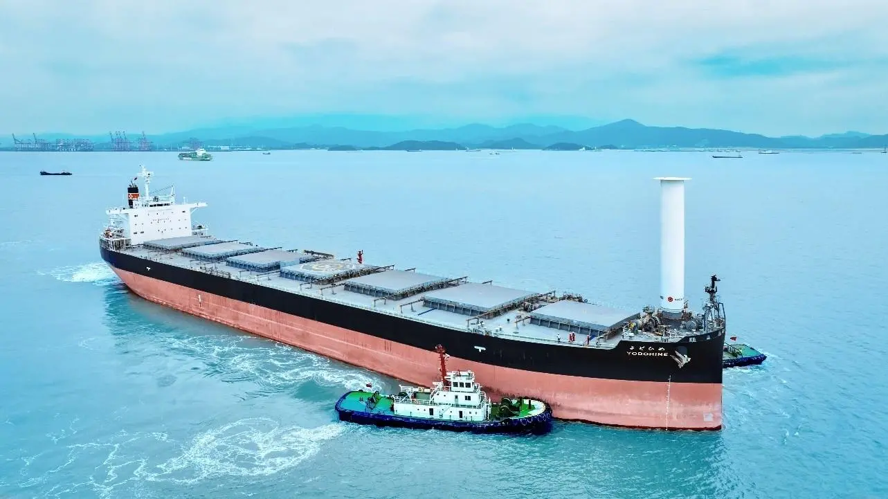Bulk carrier Yodohime at sea featuring a single Rotor Sail at its bow and a tugboat alongside