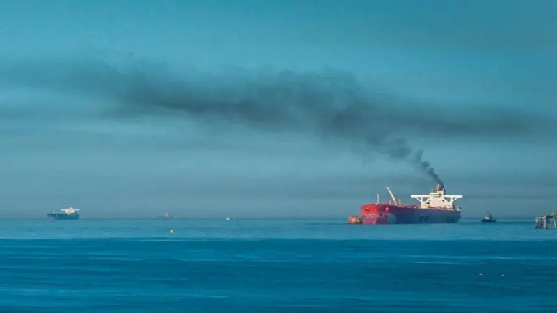 A ship at sea emitting black smoke