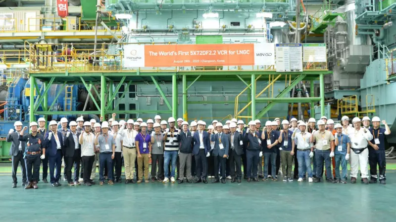 The image shows a group shot of WinGD and Hanwha Group employees in front of the LNG carrier engine