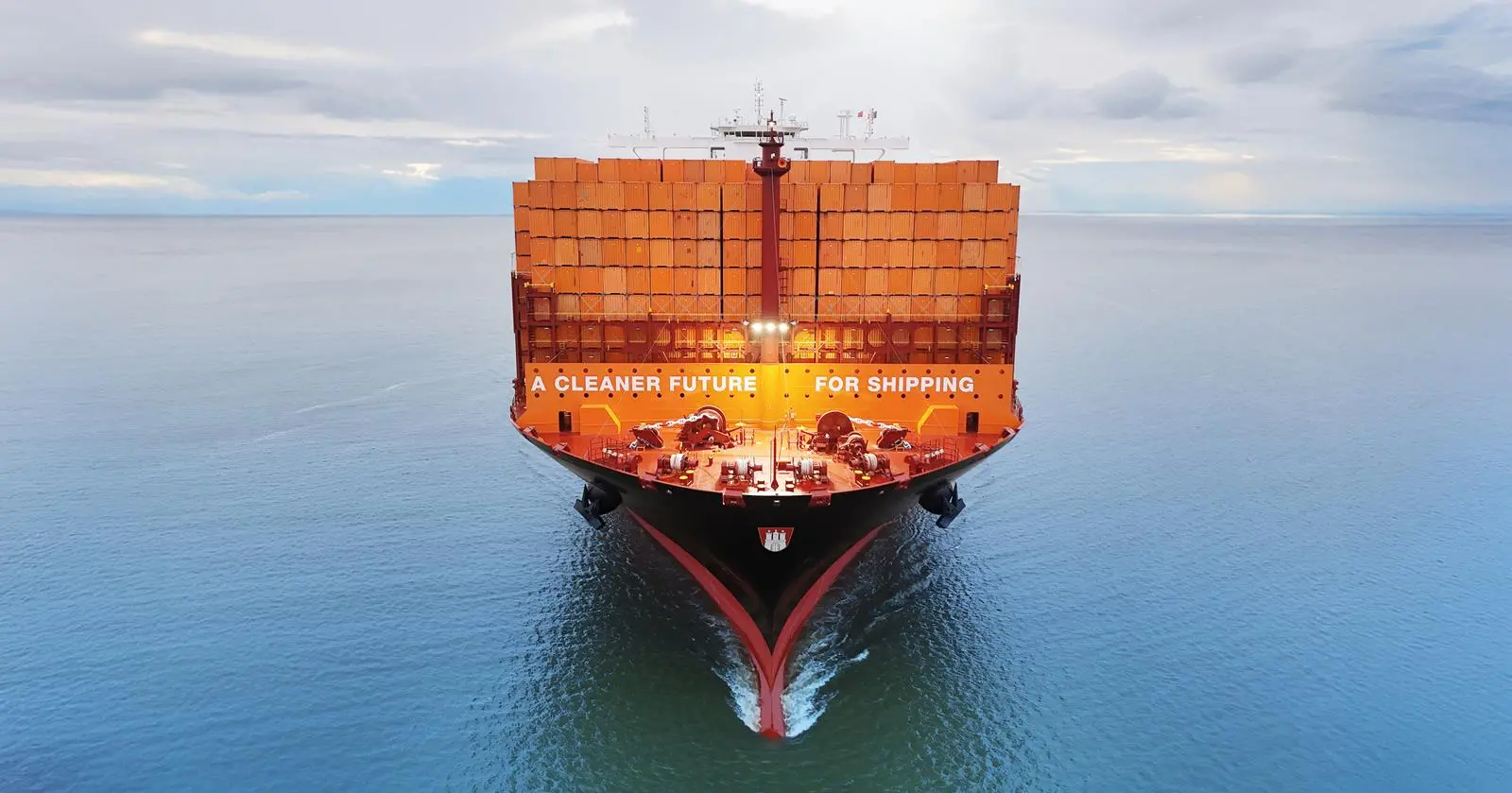 Container ship at sea full of orange containers saying 'A CLEANER FUTURE FOR SHIPPING'